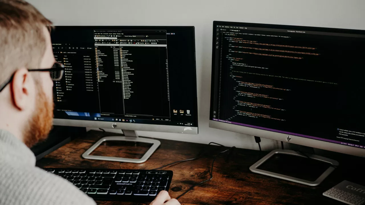 Focused software developer working on code at a modern desk setup with multiple monitors